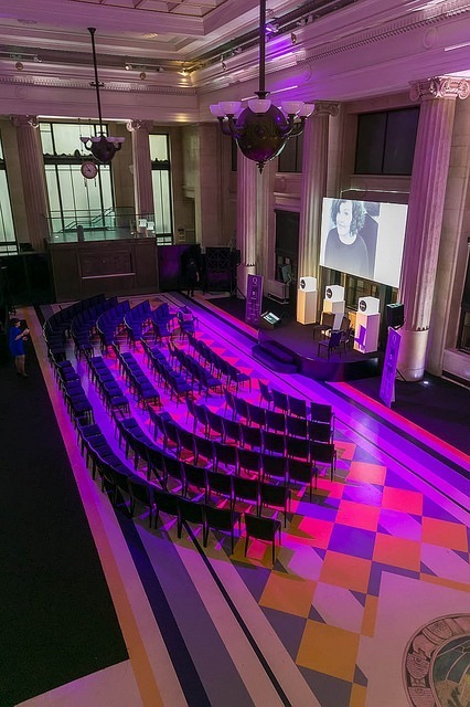 Empty conference hall with Sarah Parsonage's face projected onto a screen on stage during a One Question conference